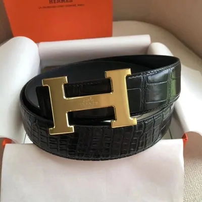 black croc-embossed leather belt with a gold buckle on its box